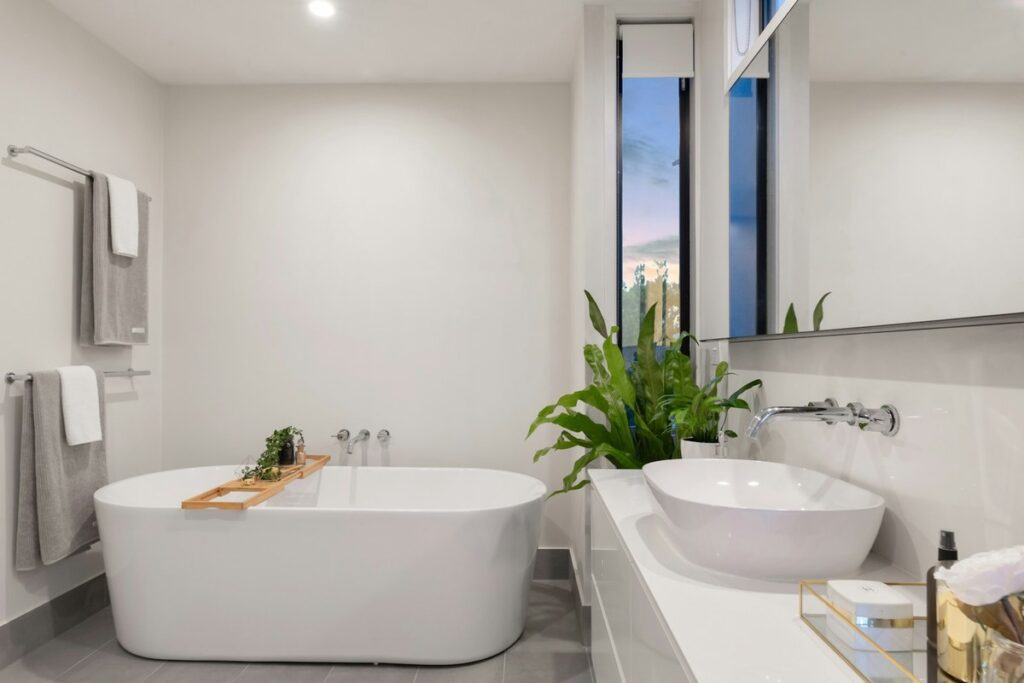 Modern minimalist bathroom with a white freestanding tub, vessel sink, and a large green plant