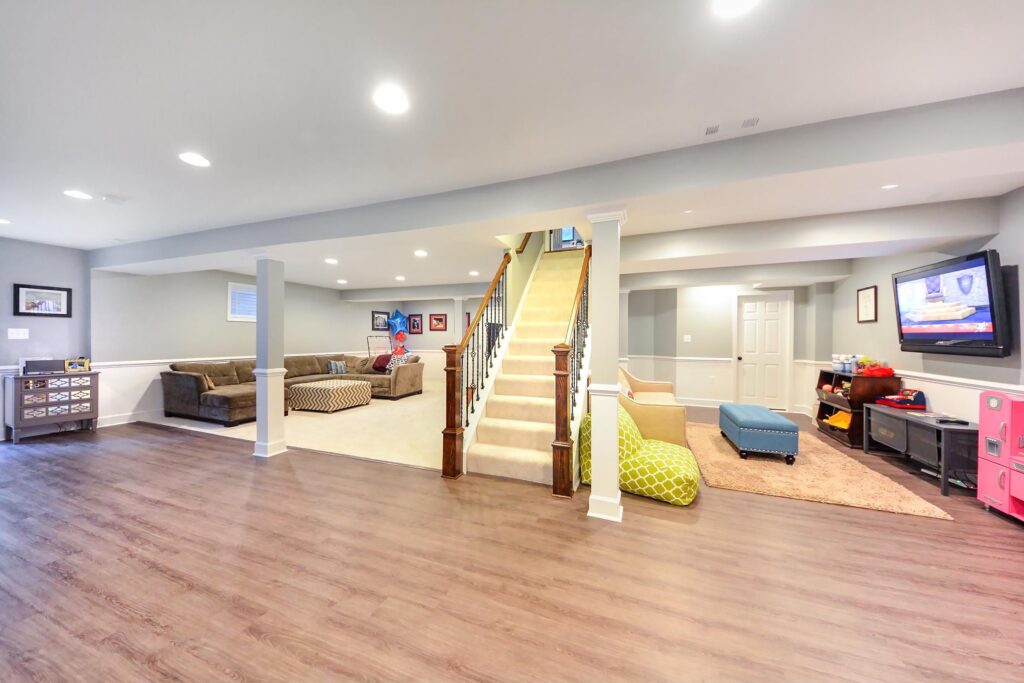 Finished basement with a central staircase, sectional sofa lounge, and a TV play area with colorful furniture