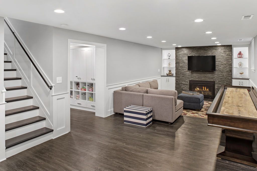 Finished basement featuring a sectional sofa, stone fireplace with a TV, shuffleboard table, and a staircase