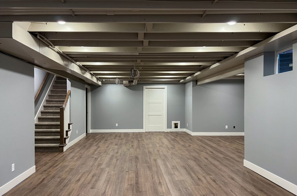 Finished basement with gray walls, wood-look flooring, exposed ceiling beams, and a staircase