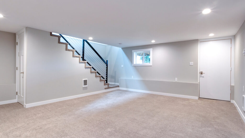 Finished basement with beige carpet, light grey walls, and a staircase with a black metal railing