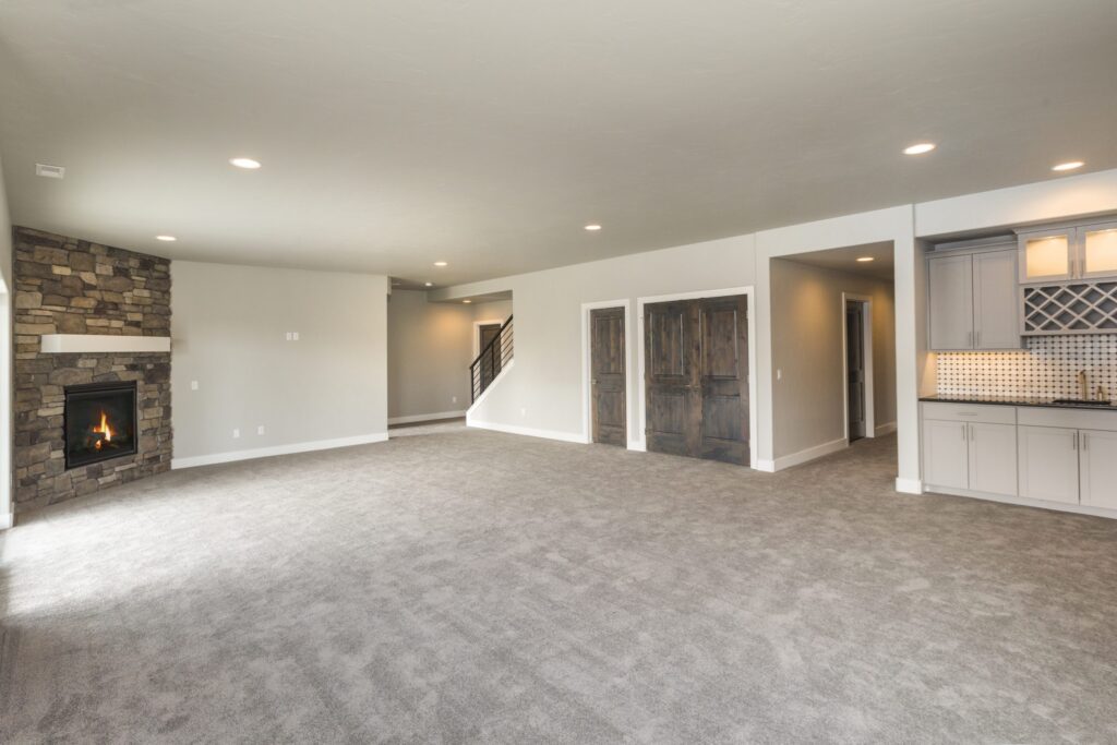 Large carpeted living area featuring a stone fireplace, a wet bar with grey cabinets, and dark wood doors