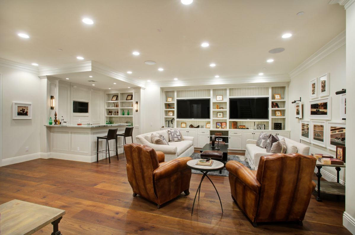Spacious living room with hardwood floors, a built-in bar, white sofas, leather armchairs, and two TVs